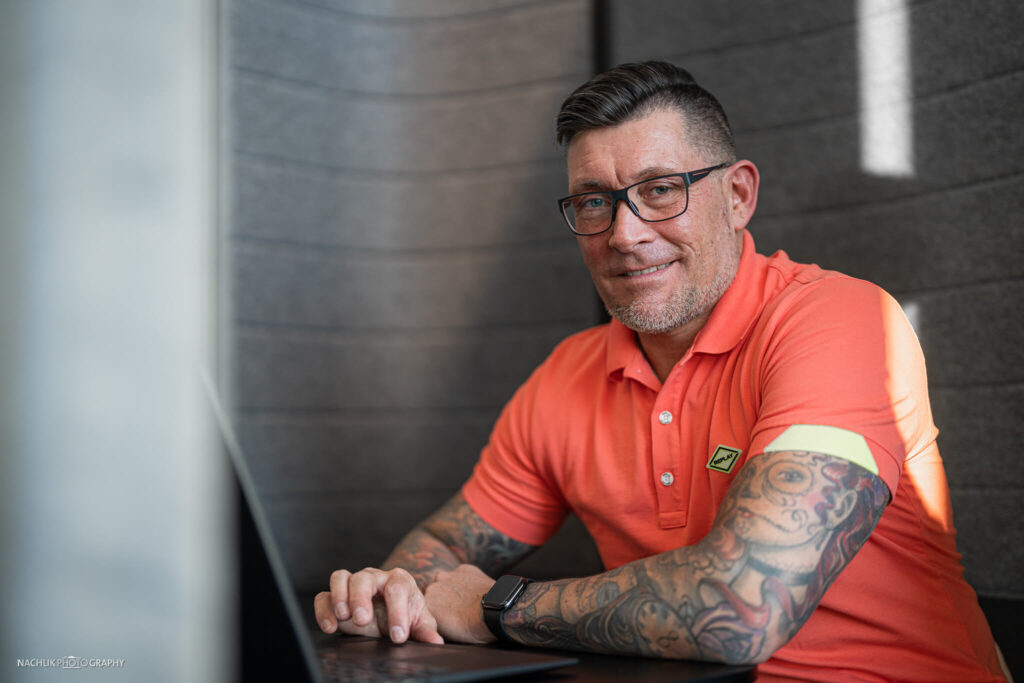 Stefan Bohn lacht in die Kamera mit orangenem T-Shirt
